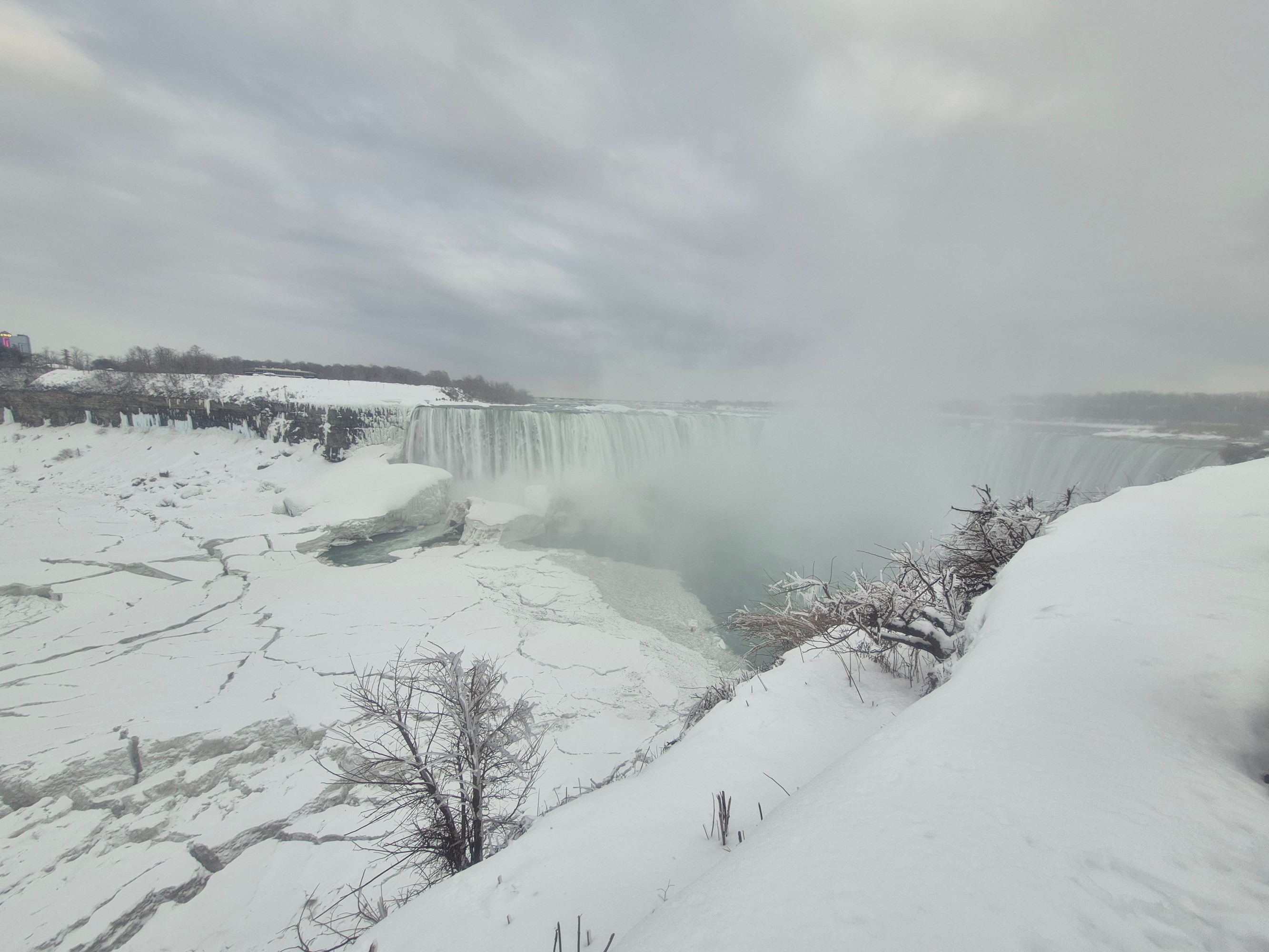 Snow-covered landscape with a large waterfall and cloudy sky.